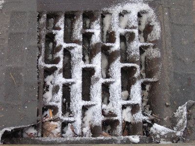 a sewer grate with a dusting of snow and purposefully obfuscated by a sheet of plastic