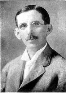 a black and white image of a man with severly parted hair, oval spectacles, winglike ears, and a mustache