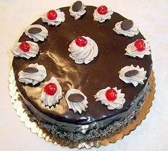 the top of a chocolate cake with dollops of whipped cream topped with chocolate coins and maraschino cherries