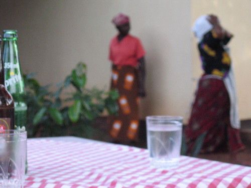 in focus, one can see a Sprite, two glasses, and a red and white checked tablecloth; in the blurry background are two women, one of whom is wearing a skirt printed with a pattern of mobile phones