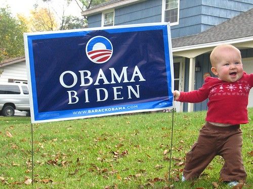 An Obama/Biden sign with a baby holding on to it