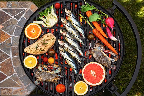 directly above a grill which has on it chicken, crab, citrus fruit, bok choy, carrots, radishes, small fish