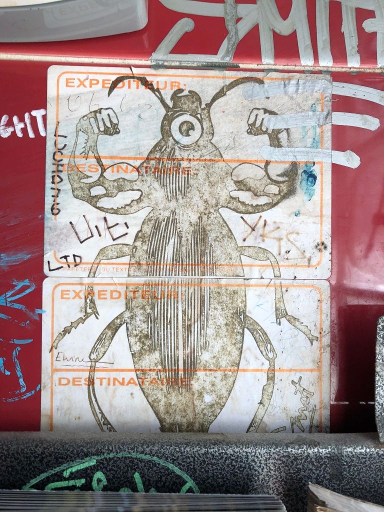 a graffiti sticker (two postal stickers together) printed with an image of a cyclopean cockroach with very muscly human arms