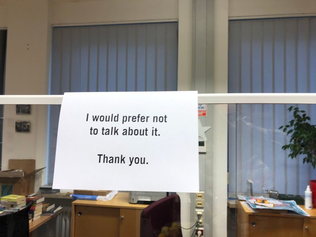 a sign hanging on the clear, plastic Corona-shield in a library upon which is printed, "I would prefer not to talk about it. Thank you."
