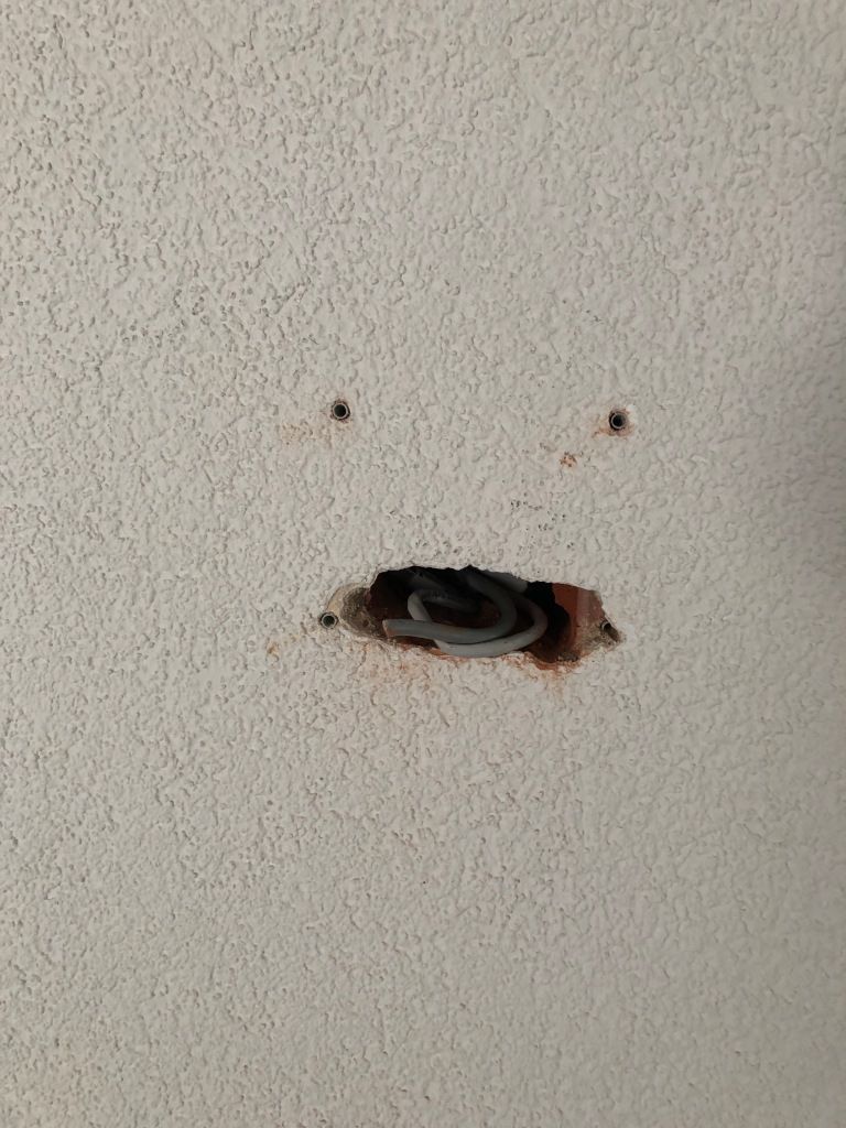 holes in a wall that look like two small eyes and a mouth with a coiled, gray tongue