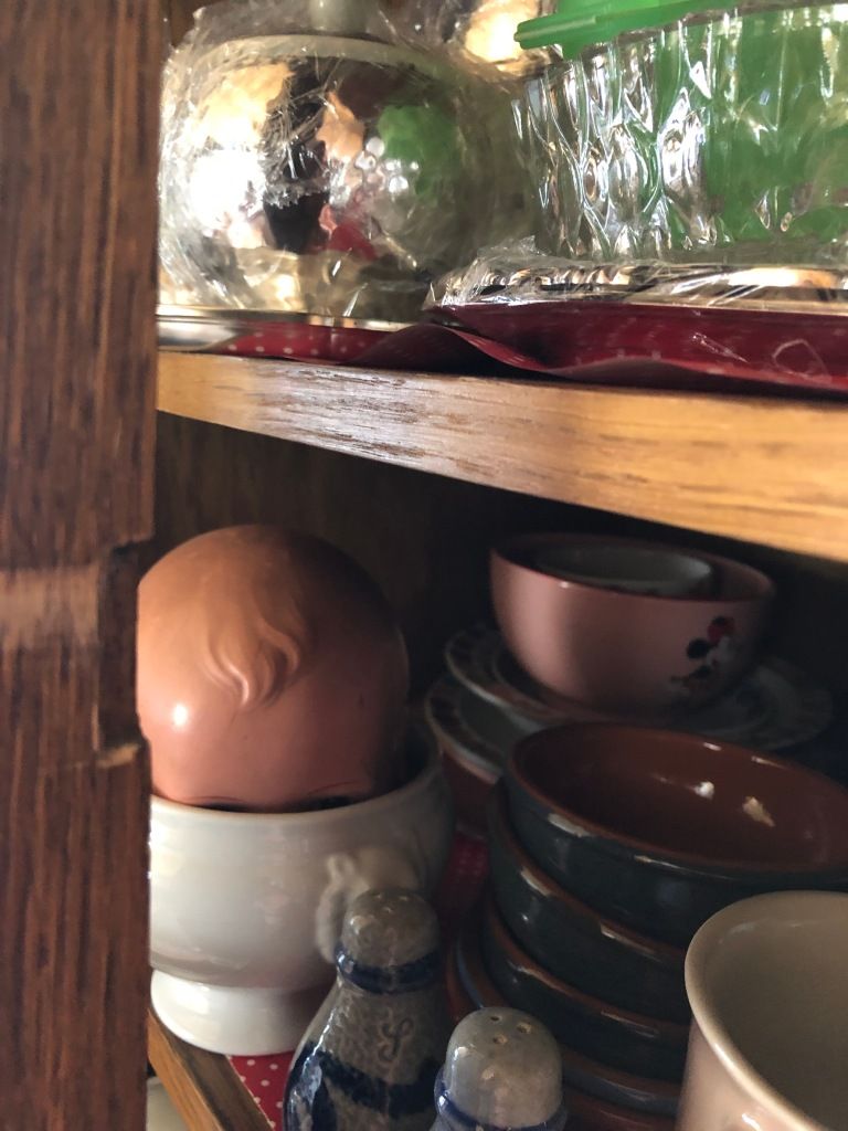the forelock of a plastic doll's head in a bowl in a hutch full of mismatched dishes