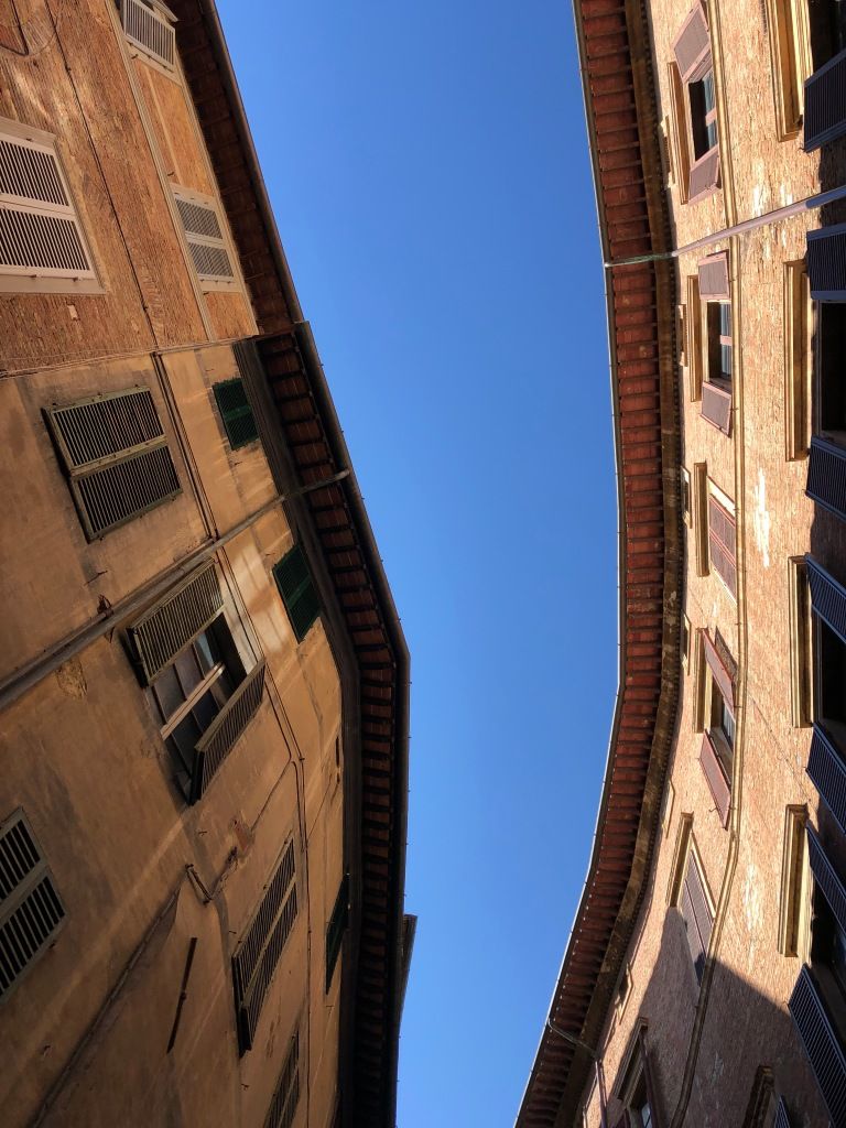 a blank blue sky as seen between the uneven curve of two buildings facing each other across a narrow street