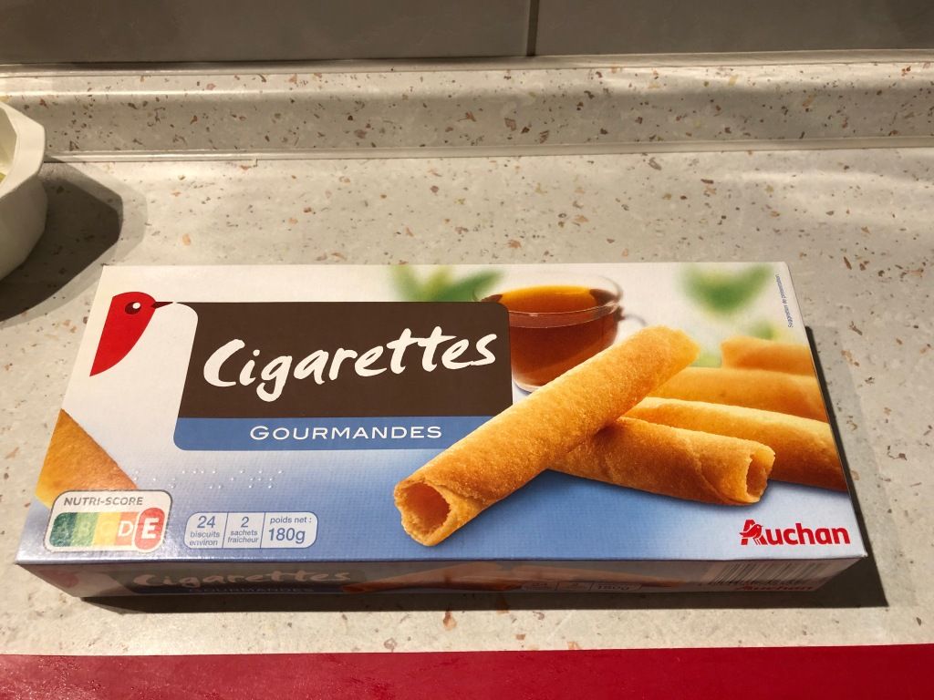 a package of rolled crepe cakes. the package shows the cakes, a cup of tea, and some blurry green shapes. a small red bird's head (the company's mascot) is speaking the name of the product: "Cigarettes GOURMANDES"