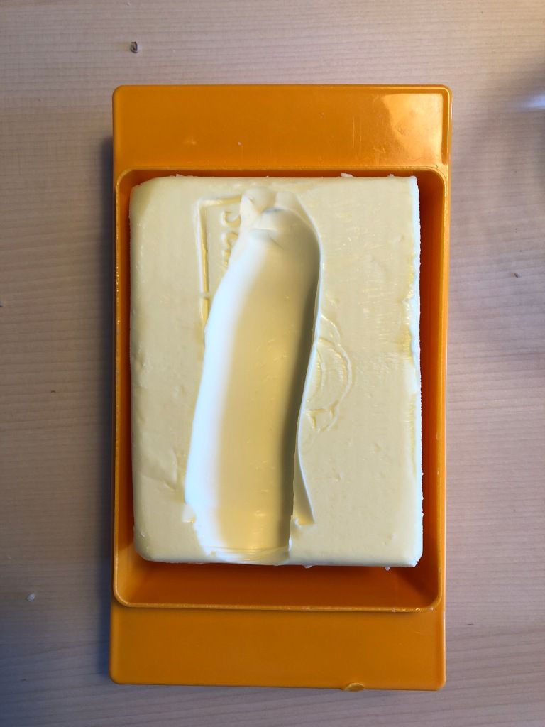 an orange plastic butter dish in which sits a brick of yellow butter out of which a great wide chunk has been spooned