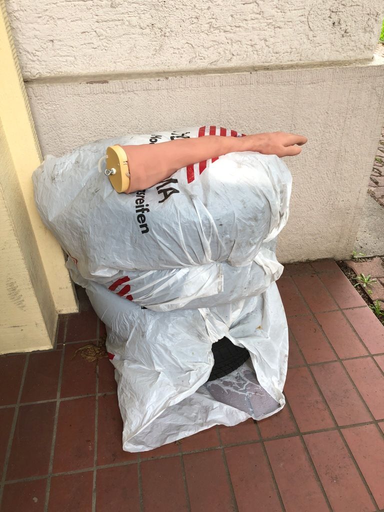 four tires wrapped in white plastic bags and stacked, upon which rests a caucasian-flesh-colored rubber arm (left) that ends just above the elbow with an eye hook.