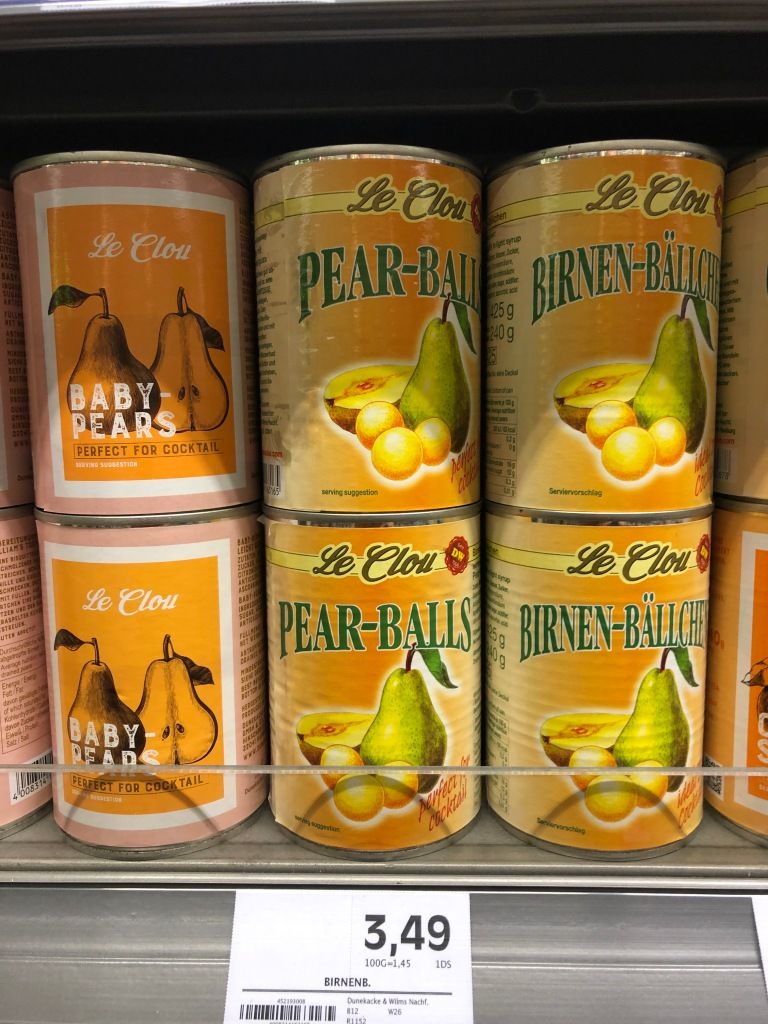 six cans of pears on a grocery store shelf. the labels of the two stacked on the left read: "Le Clou - BABY-PEARS - PERFECT FOR COCKTAIL." the labels of the two stacked in the middle read: "Le Clou - PEAR-BALLS." the labels of the two stacked on the right read: "Le Clou - Birnen-Bällchen." the two on the left have a different label than the four on the right. all of the cans cost 3.49€ each.