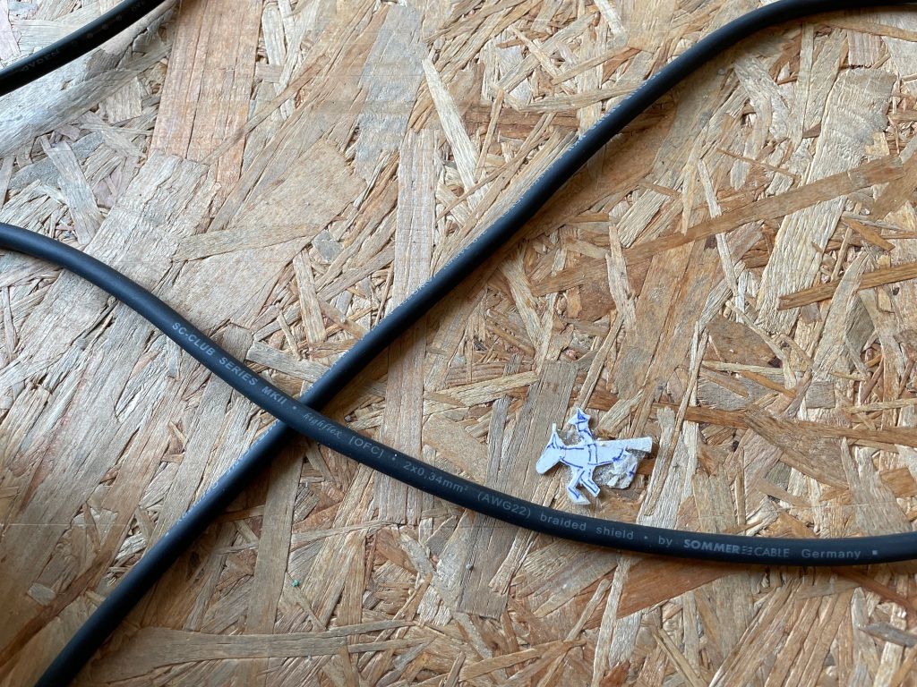 a particle board floor with three black cables criss-crossing across it and, in the lower-right curve of one of the cables, a tiny, ball-point-pen drawing of a horse and rider heading west